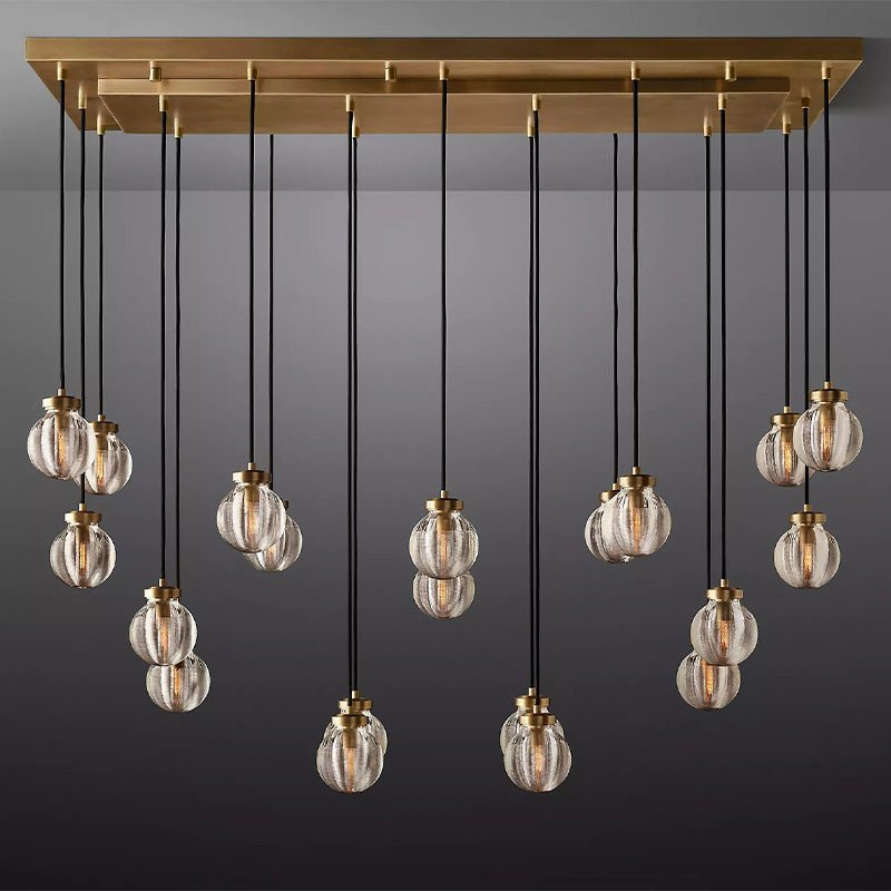 Linear chandelier with brass canopy and 16 ribbed glass globe pendants suspended by black cords against a gray background.